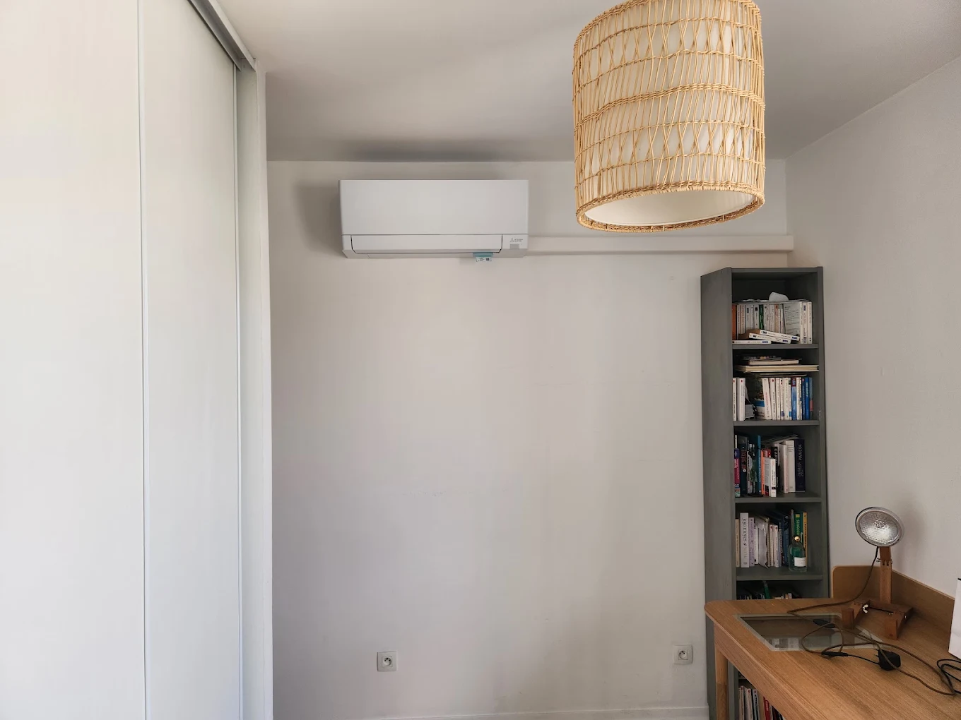 Climatisation murale et goulotte blanche dans un bureau avec bibliothèque